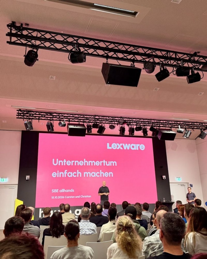 Christian Steiger auf der Bühne beim Lexware All Hands vor vollem Saal, auf der Leinwand: Unternehmertum einfach machen.